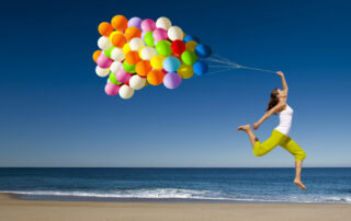 Beautiful and athletic girl with colorful balloons jumping on the beach
